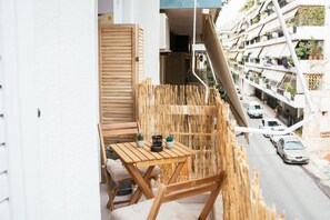 A balcony with a wooden table and chairs, a bamboo screen, and a view of a street with parked cars and buildings. - Comfy stay 2br flat 1gbps 4 min walk from metro (Athina)