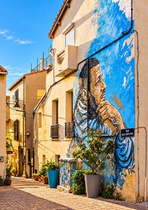 Un carrer estret amb un mural a un edifici, plantes en testos i un senyal que diu 'RUE DES DEPUTES'.