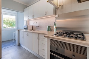 A modern kitchen with white cabinets, a stainless steel stove, and a window providing natural light. - Apartment 'Lisbon Oceanside' (Carcavelos)