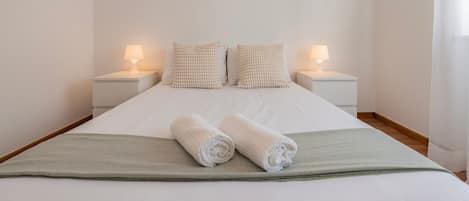 A neatly made bed with two pillows and two rolled towels, flanked by bedside tables with lamps.
