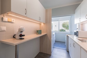 Une cuisine moderne avec des armoires blanches, un four encastré et une fenêtre donnant sur l’extérieur.