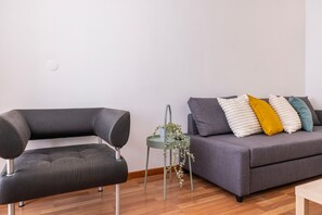 Ein modernes Wohnzimmer mit einem grauen Sofa, einem schwarzen Sessel und einem kleinen Tisch mit einer Pflanze.