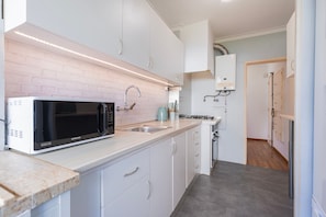 A modern kitchen with white cabinets, a black microwave, and a stainless steel sink. - Apartment 'Lisbon Oceanside' (Carcavelos)