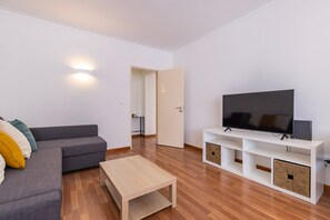 A modern living room with a grey sofa, a coffee table, a flat-screen TV on a white stand, and a wooden floor. - Apartment 'Lisbon Oceanside' (Carcavelos)