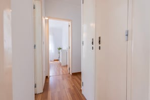 Ein Flur mit Holzdielen und weißen Wänden, der zu einem Zimmer mit Pflanze und Tür führt.