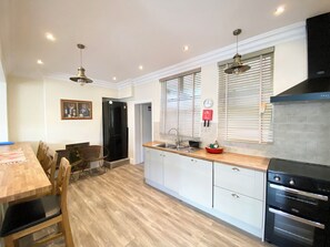 A modern kitchen with white cabinetry, a wooden dining table, and a black range hood. - Nesden House (Looe)