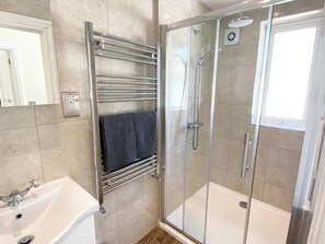 A modern bathroom with a glass shower enclosure, a white bathtub, and a towel rack with a dark towel. - Nesden House (Looe)