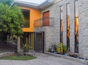 Una casa moderna de dos pisos con fachada de piedra, un balcón con barandilla de hierro forjado y un jardín bien cuidado.