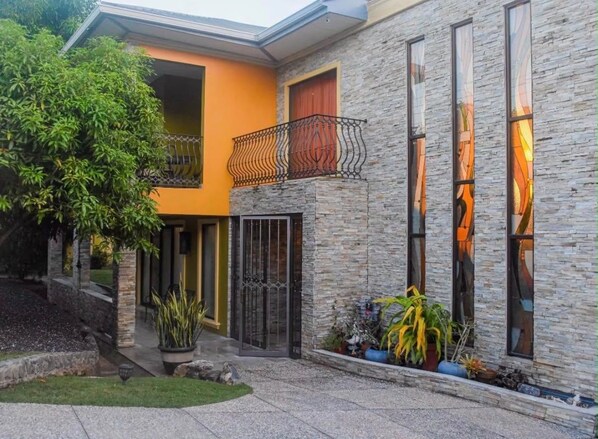 Een modern herenhuis met twee verdiepingen, een gevel van natuursteen, een balkon met ijzeren hekwerk en een verzorgde tuin.