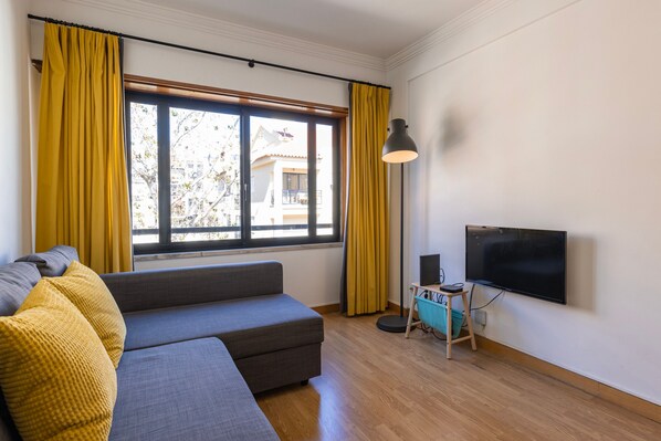 A modern living room with a grey sofa, yellow cushions, a flat-screen TV, and a floor lamp. - Apartment 'Cozy Carcavelos Apartment' (Carcavelos)