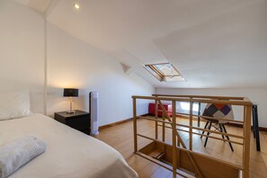A bedroom with a bed, bedside table, lamp, heater, and a view of a balcony with a chair and a red cabinet. - Apartment 'Cozy Carcavelos Apartment' (Carcavelos)
