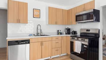 Eine moderne Küche mit Holzausstattung, einem Edelstahl-Geschirrspüler, einem schwarzen Backofen und einer Mikrowelle.