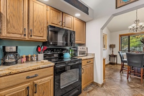 A kitchen with wooden cabinets, a black stove, a microwave, and a coffee maker. - NEW! | Rustic Woodland Retreat | Pets | Fireplace (Flagstaff)