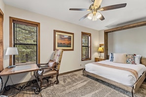 A bedroom with a bed, a desk, a chair, a ceiling fan, and two windows with blinds. - NEW! | Rustic Woodland Retreat | Pets | Fireplace (Flagstaff)