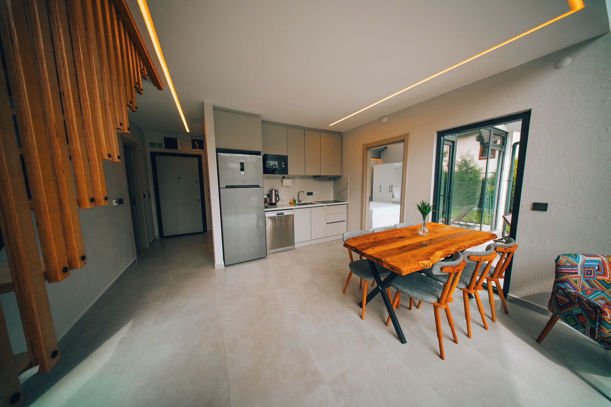 A modern kitchen with a dining area, featuring a wooden table and chairs, a refrigerator, and a microwave.