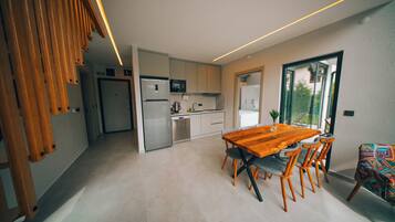A modern kitchen with a dining area, featuring a wooden table and chairs, a refrigerator, and a microwave.