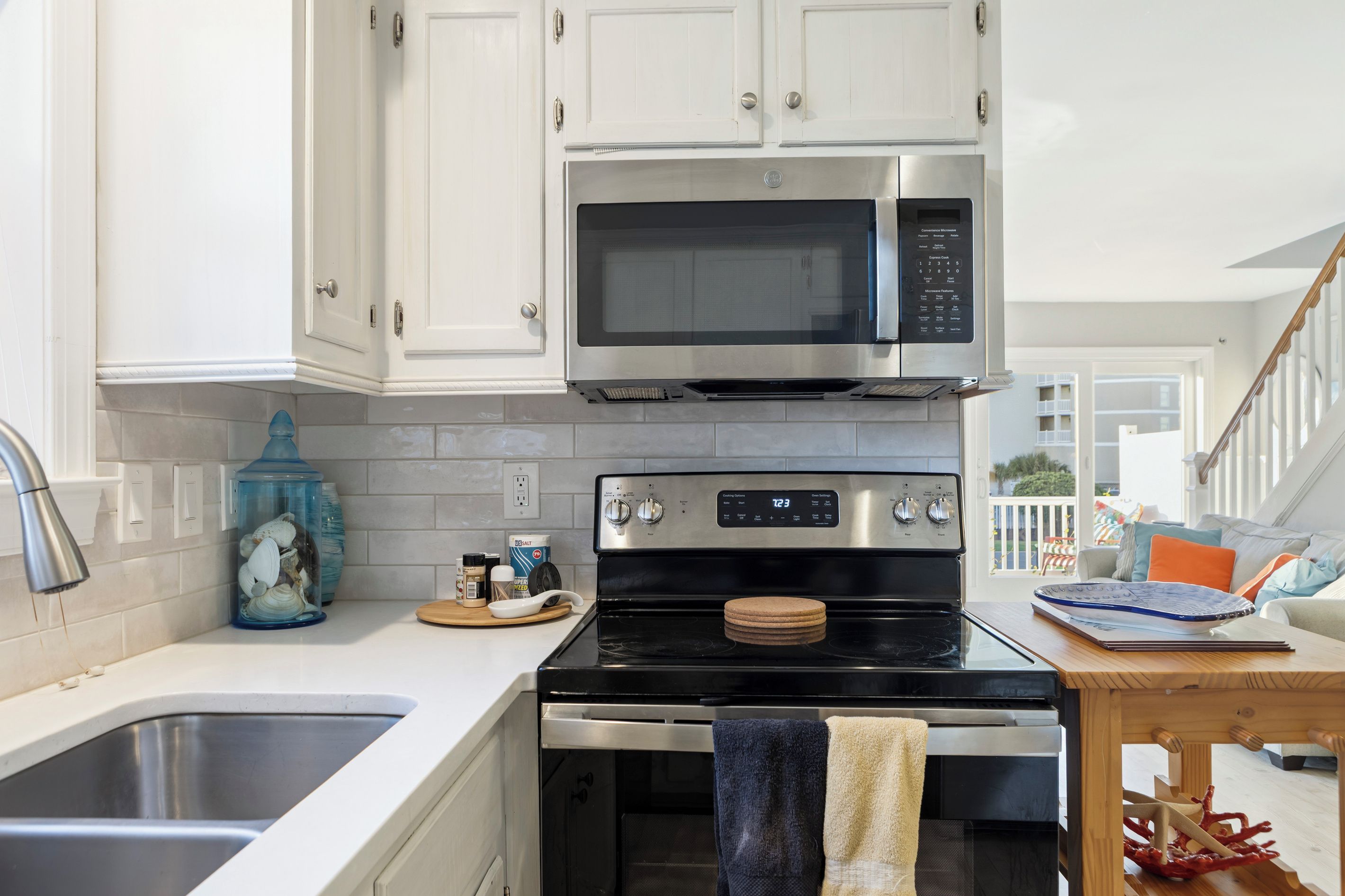 A kitchen with white cabinets, a stainless steel microwave, a stove, and a sink.