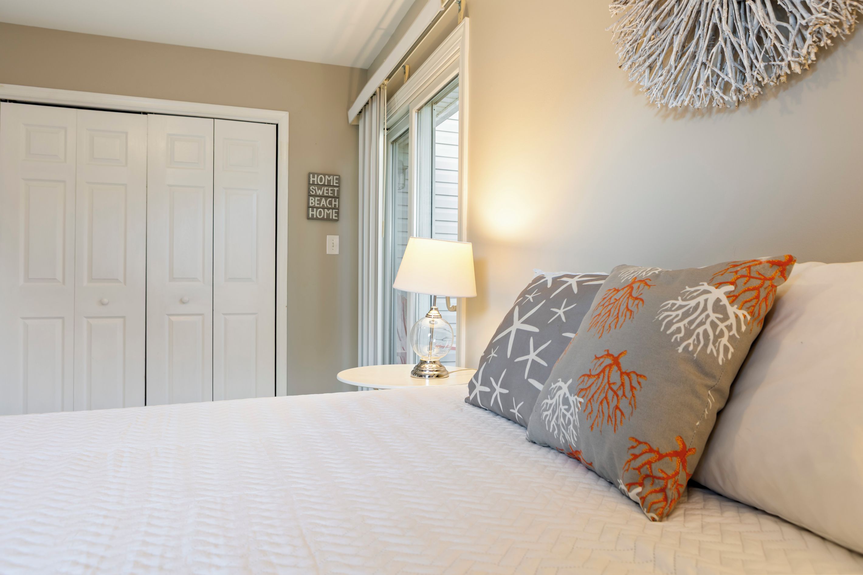 Un dormitorio con cama, mesita de noche con lámpara, ventana con persianas y decoración en la pared.