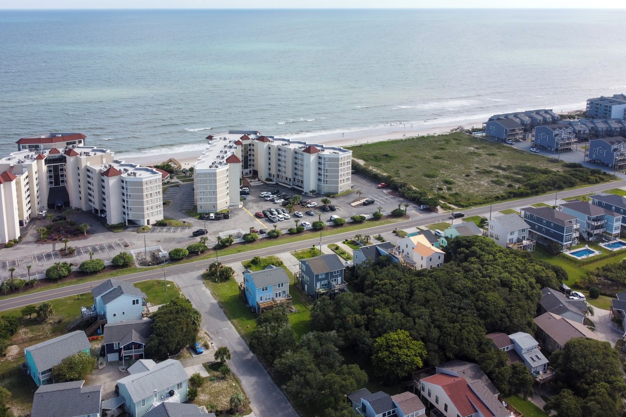 A coastal residential area with beachfront properties, a parking lot, and a road leading to the beach.