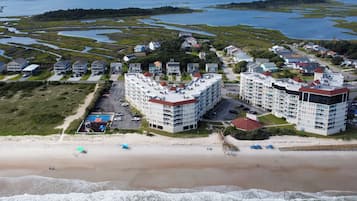 Un quartier résidentiel situé sur la côte, avec des propriétés donnant sur la plage, notamment des immeubles à plusieurs étages avec des toits rouges et une plage parsemée de parasols.