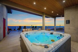 Uma banheira de hidromassagem com vista para o pôr do sol, área de estar externa e teto de madeira.