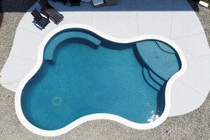 Ein Swimmingpool mit einem einzigartigen Wellenranddesign, umgeben von einer gefliesten Sonnenterrasse.