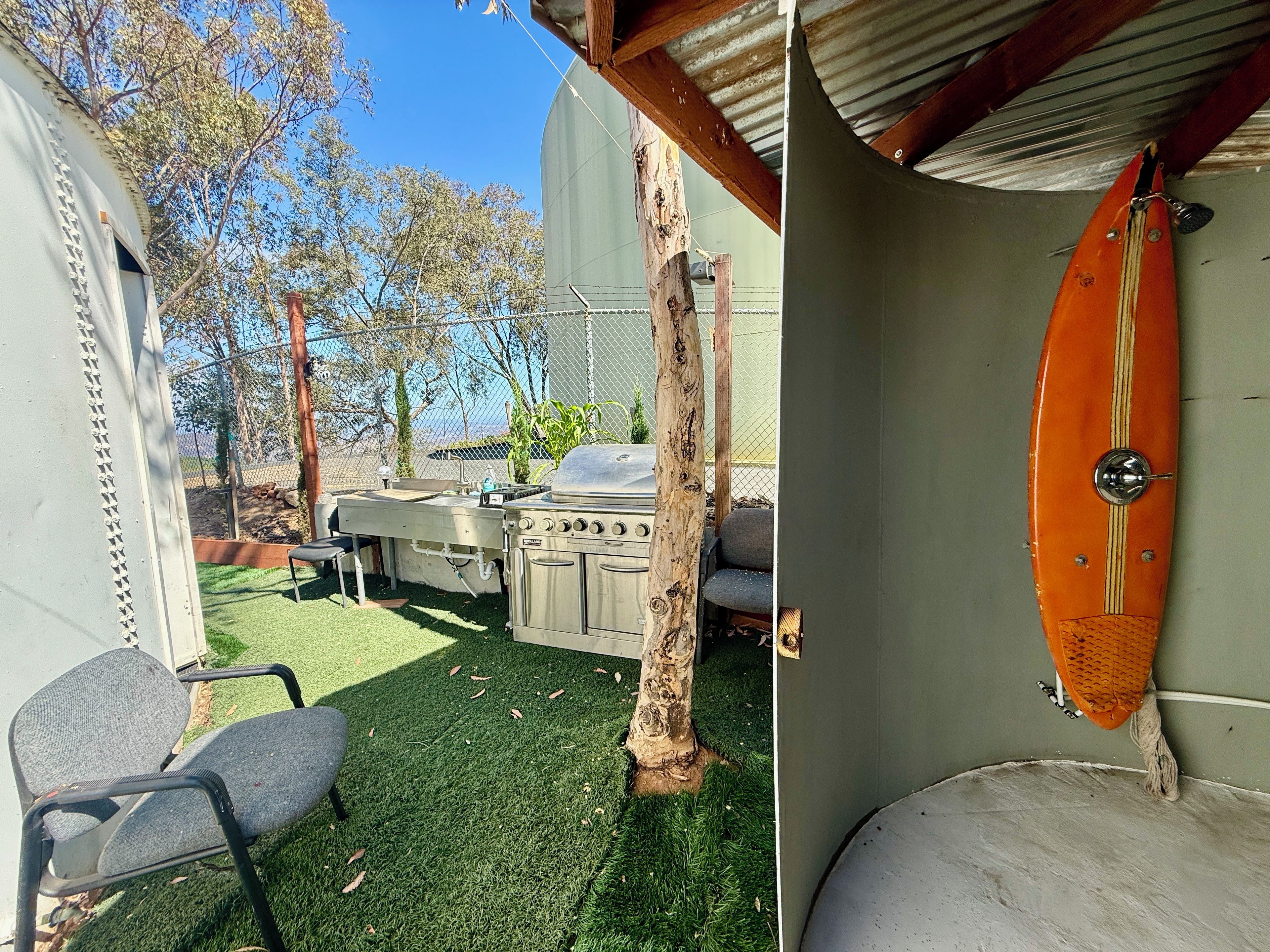 A covered outdoor area with a grill, chairs, and a surfboard.