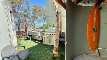 A covered outdoor area with a grill, chairs, and a surfboard.