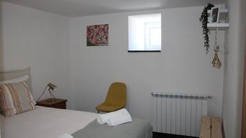 A bedroom with a bed, a chair, a radiator, a window, and a wall-mounted shelf with a plant.