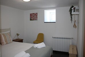 Un dormitorio con una cama, una silla, un radiador, una ventana y una estantería con una planta.