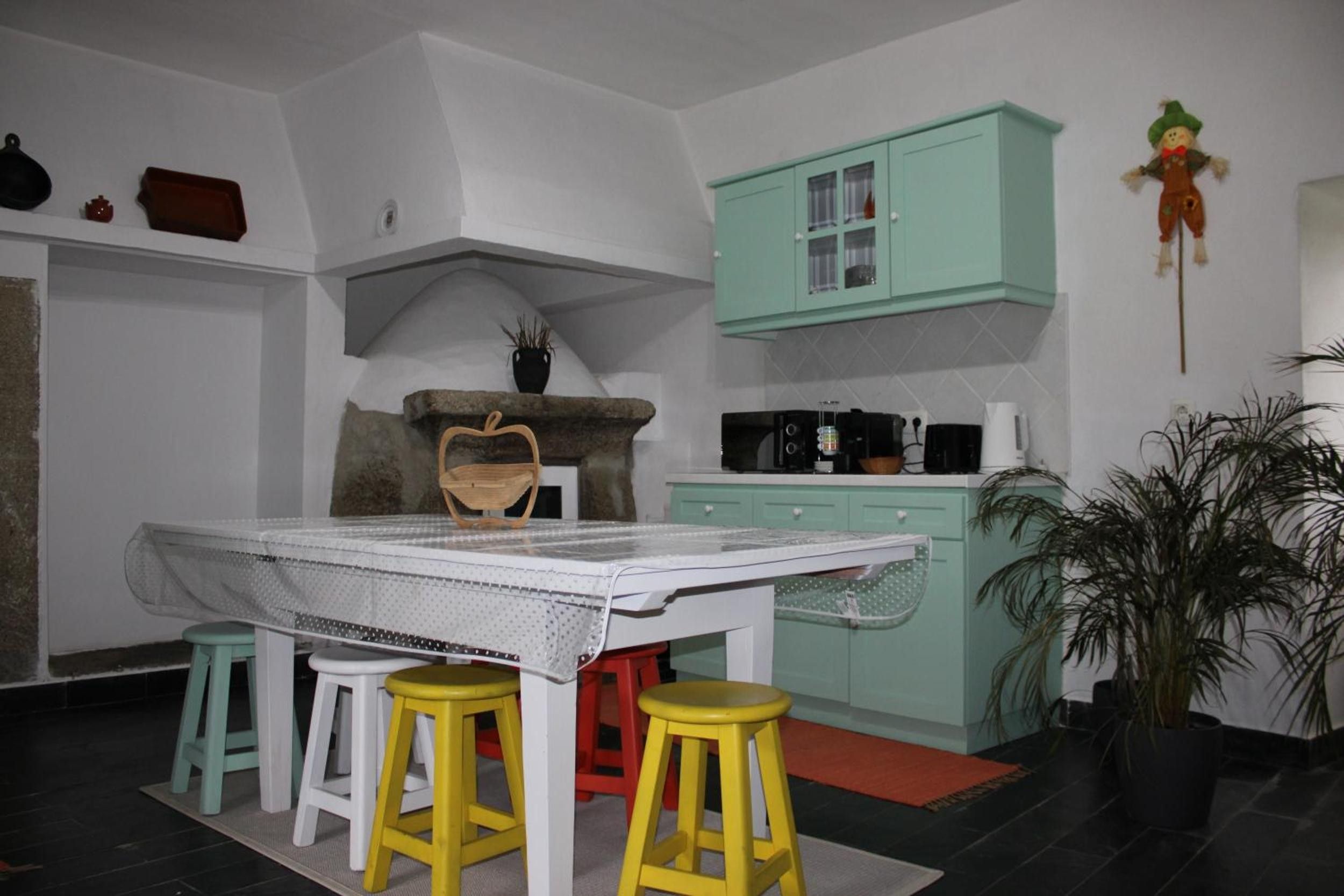Une cuisine avec une table blanche, des tabourets jaunes, un meuble vert et une plante en pot.