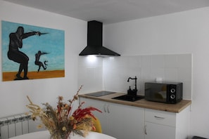 A kitchen with a black range hood, a microwave, and a sink. There's a painting on the wall and a vase with dried flowers on the counter.