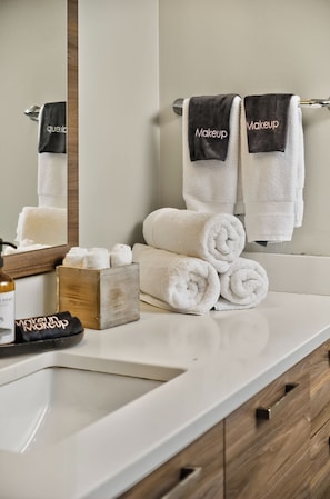 A bathroom with a white sink, wooden cabinets, and two towels hanging on a towel rack with the word "Makeup" on them. - The Bentley Collection - The Vinyl Loft (Dallas)