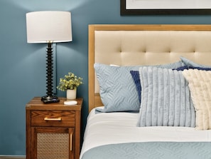 A bedroom with a bed, a nightstand with a lamp, a small plant, and a framed picture on the wall. - The Bentley Collection - The Vinyl Loft (Dallas)