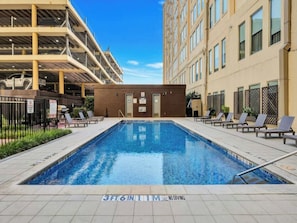 A swimming pool with lounge chairs, a building with multiple floors, and a clear sky. - The Bentley Collection - The Vinyl Loft (Dallas)