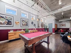 A pool table in a room with wooden flooring, pendant lighting, and wall-mounted artwork. - The Bentley Collection - The Vinyl Loft (Dallas)
