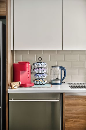 A kitchen counter with a red coffee maker, a coffee cup, a stack of coffee pods, and a blue electric kettle. - The Bentley Collection - The Vinyl Loft (Dallas)