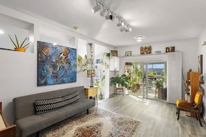 A spacious living area with a grey sofa, a large abstract painting, and a variety of plants.