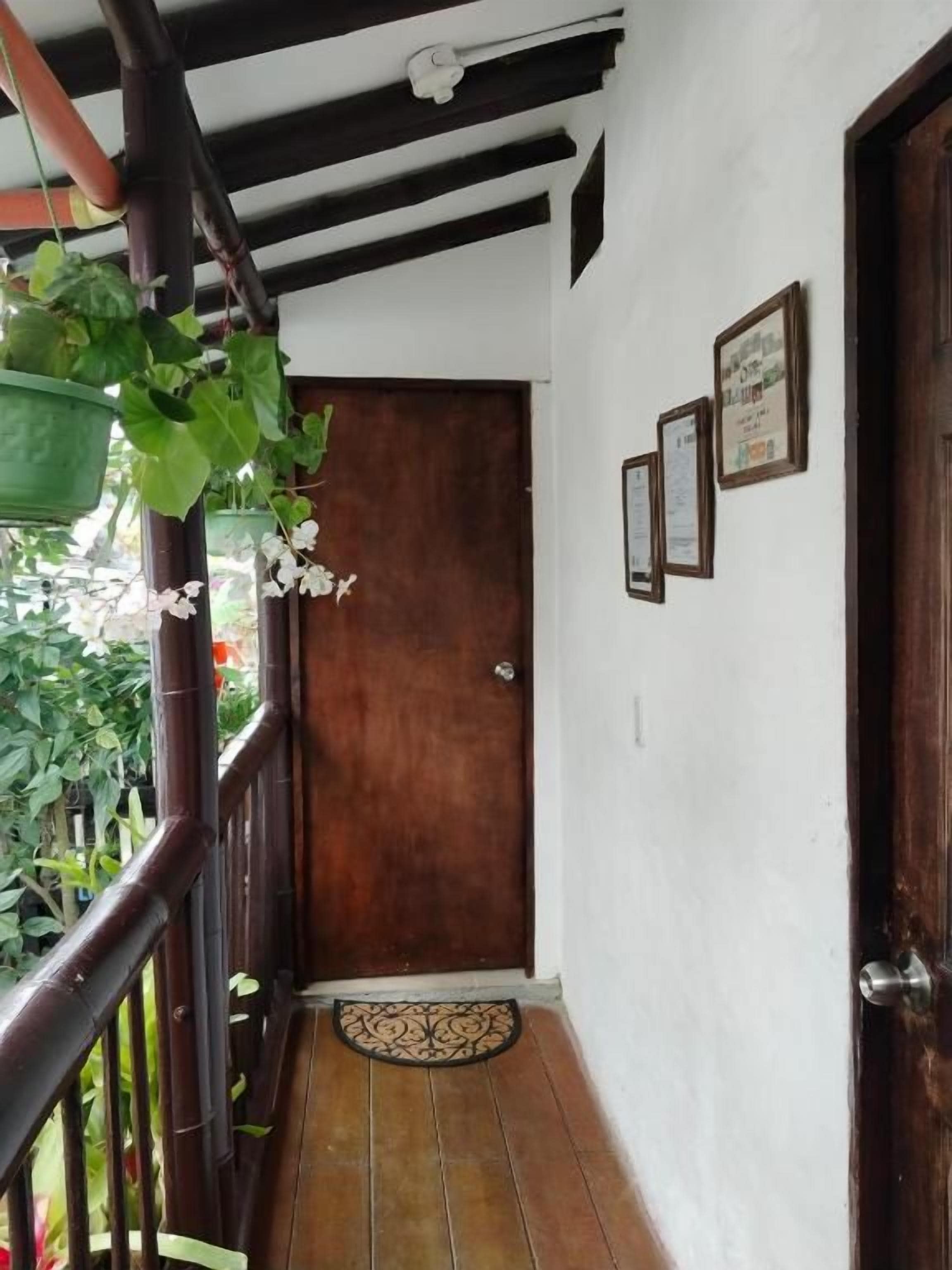 Un estrecho pasillo de madera con una puerta al final, un felpudo pequeño en la entrada y una barandilla metálica a un lado.