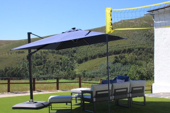 An outdoor seating area with a table and chairs, a patio umbrella, and a view of a hilly landscape.