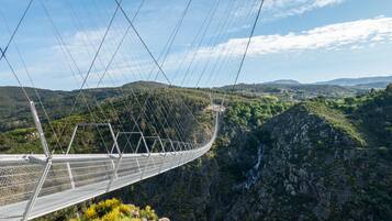 A suspension bridge with a metal framework and safety railings, spanning a deep gorge with a waterfall below.