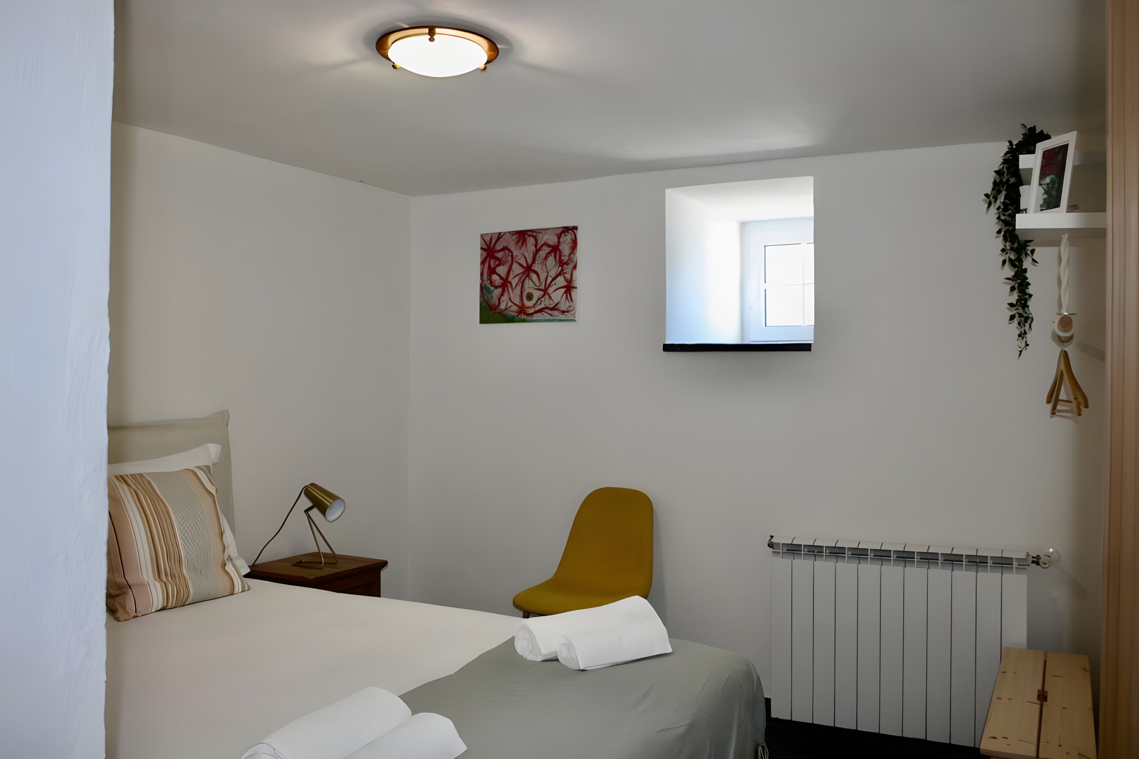 A bedroom with a bed, a nightstand, a chair, a radiator, and a window.