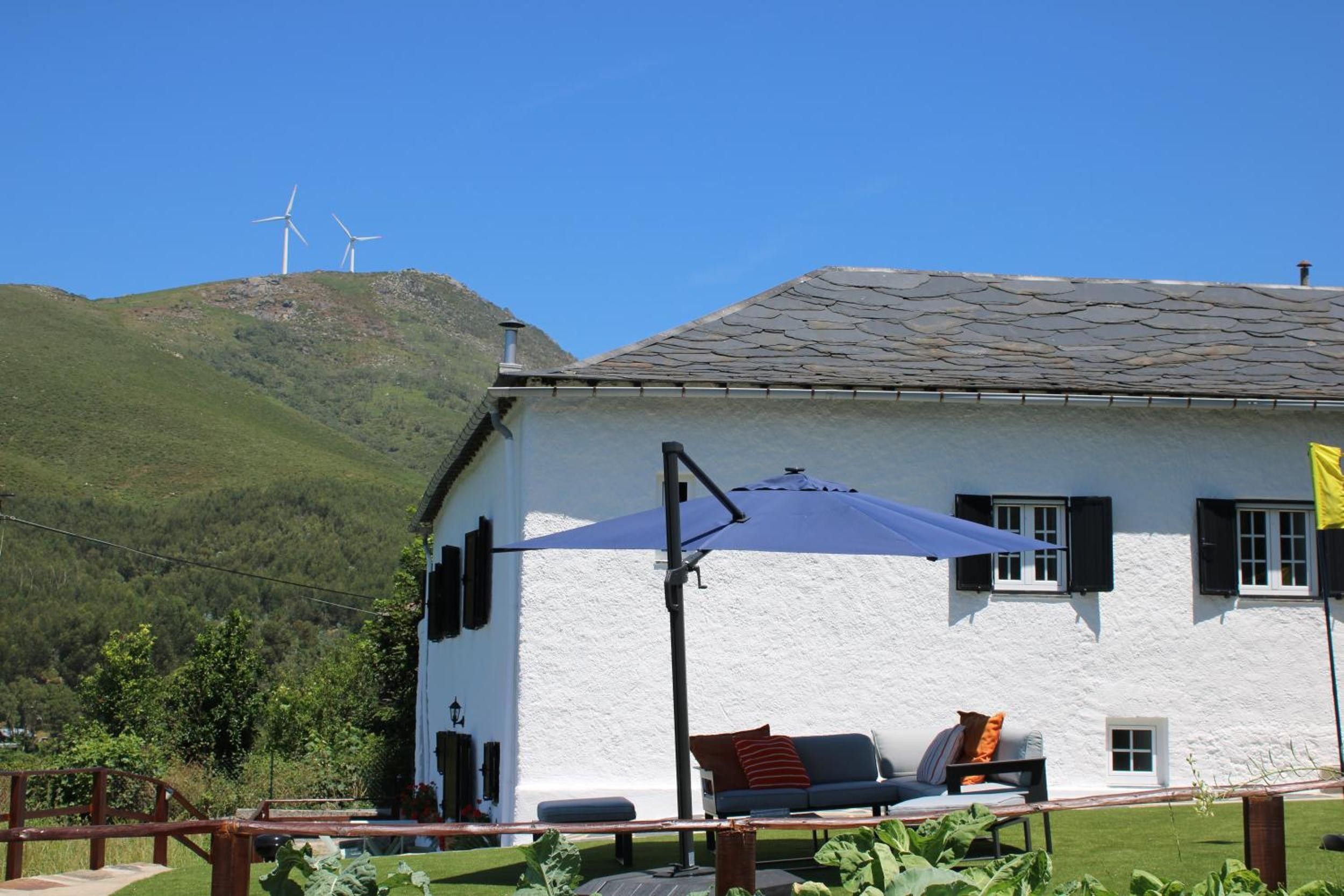 A white building with a stone roof, a blue umbrella, and a sofa with cushions.
