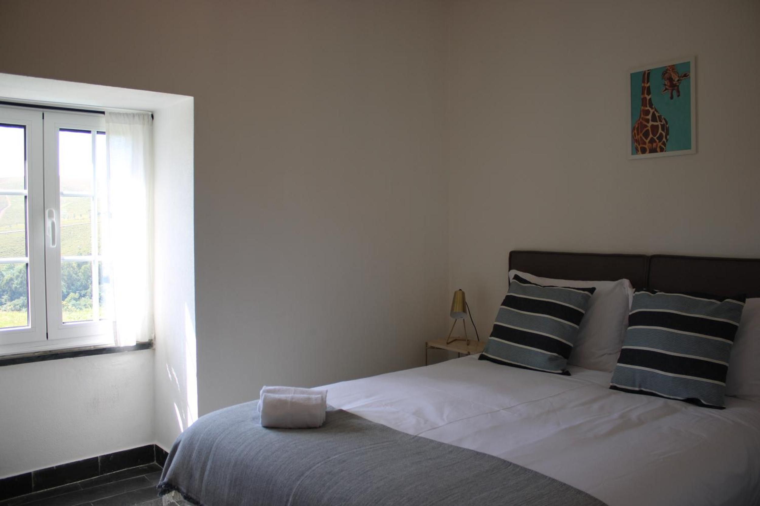 A bedroom with a bed, a nightstand, a lamp, and a window.