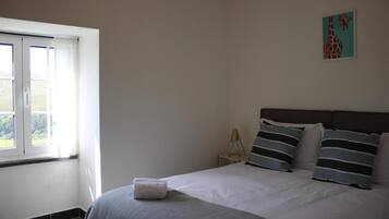 A bedroom with a bed, a nightstand, a lamp, and a window.