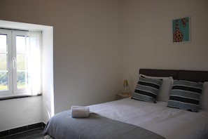 Un dormitorio con cama, mesita de noche, lámpara y ventana.