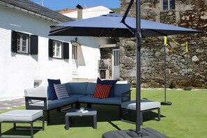 A modern outdoor seating area with a blue umbrella, a white building, and a stone wall in the background.