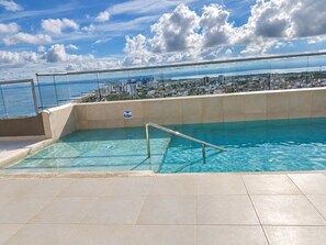 Ein Pool auf dem Dach mit Glasumrandung und Blick auf die Stadt.