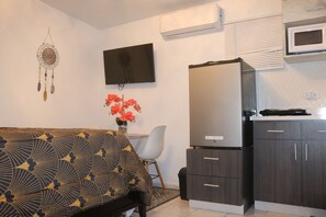 A compact living space with a sofa, a flat-screen TV, a refrigerator, and a microwave. - Segovia Room—Near the Airport (Carolina)