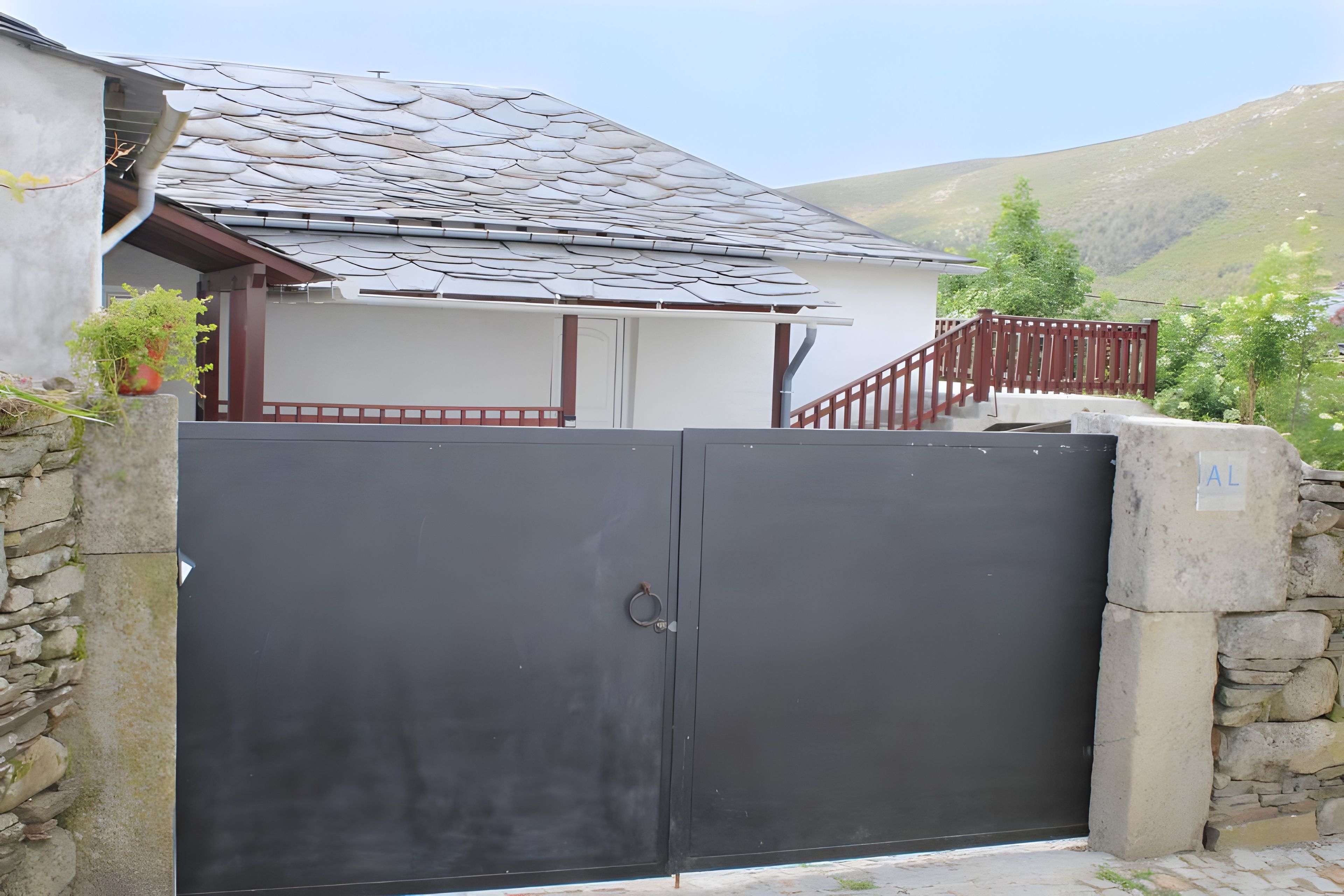 Une propriétéClose, entourée d’un mur de pierre, dotée d’un portail en métal et d’un escalier menant à un bâtiment dont le toit est recouvert de tuiles.